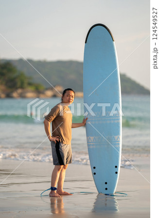 Smart Asian Man long hair touches and poses with Standed Surfboard on the beach in Twilight time Smart Asian Man long hair touches and poses with Standed Surfboard on the beach in Twilight time 124549527