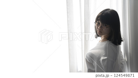 Asian Thai Chinese Woman with her black glasses stands in front of white curtain with the light from outside. It's a cute sexy shot image. 124549871