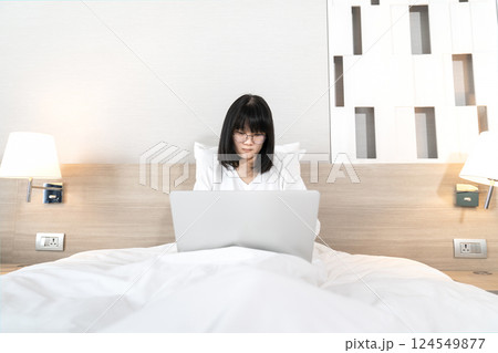 Glasses Asian cute woman works and plays laptop notebook on the bed in Work From Home period. Glasses Asian cute woman works and plays laptop notebook on the bed in Work From Home period. 124549877