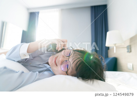 Asian young glasses woman talk to the mobile phone while lie on her side on the bed in the morning. Asian young glasses woman talk to the mobile phone while lie on her side on the bed in the morning. 124549879