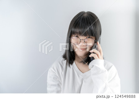Isolated Pretty Asian glasses woman talks and speaks in the line with her mobile phone on white background in studio light. 124549888