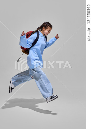 Girl with backpack joyfully leaps forward, ready for new adventures and knowledge awaiting on back to school day. Education concept. Girl with backpack joyfully leaps forward, ready for new adventures and knowledge awaiting on back to school day. Education concept. 124550560