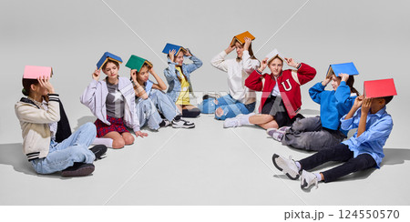 Group of students sit in circle with books balanced on heads, looking up, representing fun and imaginative approach to study. Knowledge day concept. 124550570
