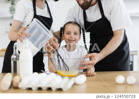 Happy Caucasian family cooking in kitchen, parents helping daughter whisk eggs for baking 124550728