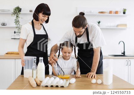 Caucasian family, including parents and child, cooking in modern kitchen together, whisking ingredients. 124550733
