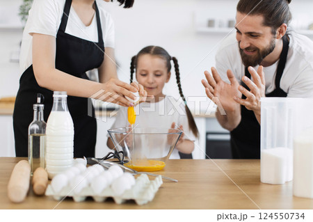 Caucasian family showing father, mother, and young daughter cooking meal in kitchen setting. Family bonding, cooking, and culinary learning captured with enthusiasm, teamwork, and togetherness. 124550734