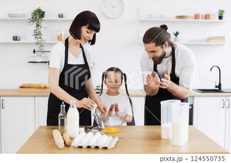 Caucasian family cooking in kitchen, happy parents and child preparing meal together, illustrating love and care. 124550735