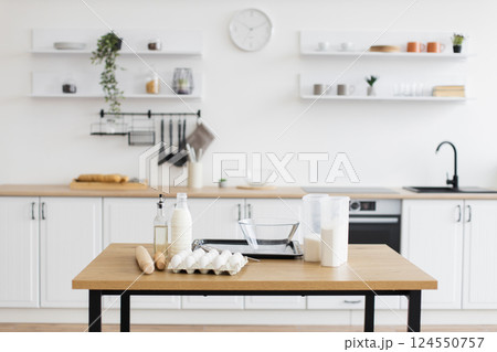 Bright contemporary kitchen containing minimalist decor and baking essentials such as eggs, milk, and flour on table, emphasizing simplicity and readiness for cooking or baking. 124550757