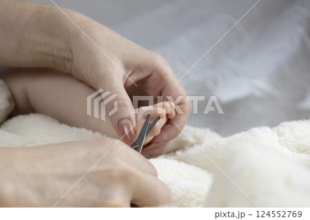 Mom trims baby's nails with baby scissors. Close up photo of mother's hands holding feet of the infant and nail scissors. Mom trims baby's nails with baby scissors. Close up photo of mother's hands holding feet of the infant and nail scissors. 124552769