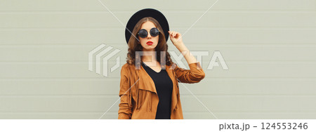 Beautiful stylish young woman posing in black hat, jacket, glasses on gray background 124553246