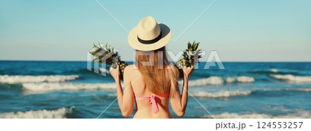 Summer vacation, beautiful young woman in bikini swimsuit, hat, pineapple fruits on the beach at sea 124553257