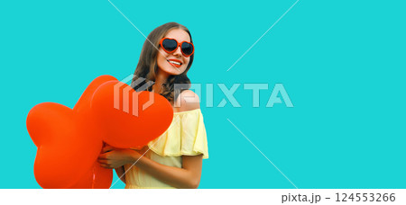 Happy smiling young woman with red heart shaped balloon on blue studio background 124553266