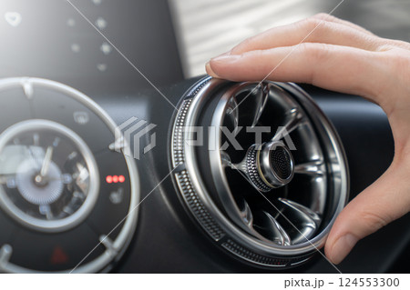 A hand gently adjusts a sleek and stylish car air vent to ensure optimal comfort and effective climate control. Making adjustments to the car air conditioning vent for optimal comfort and efficiency 124553300