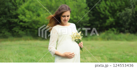 Pregnancy, maternity, happy young pregnant woman holding bouquet of flowers standing in summer park 124553436