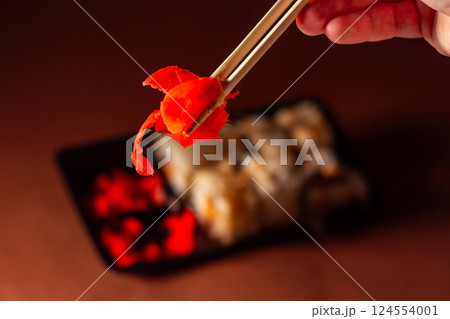 Chopsticks taking portion of sushi roll. Sushi rolls with salmon cream cheese and cucumber in take away package. Food delivery concept. 124554001