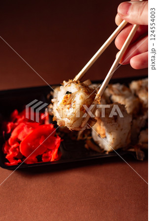 Hand with chopsticks taking portion of sushi roll. Sushi rolls with salmon cream cheese and cucumber in take away package. Food delivery concept. 124554003