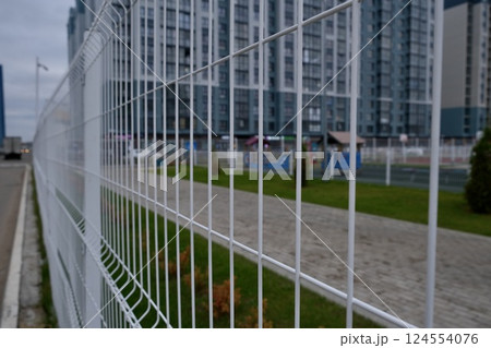 A close-up view of a white fence in an urban setting, with modern buildings behind it, showcasing a contemporary city vibe A close-up view of a white fence in an urban setting, with modern buildings behind it, showcasing a contemporary city vibe 124554076