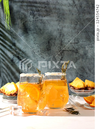 Summer party concept. Tequila, rum and vodka cocktail with pineapple slices, orange, ice and rosemary. Diet drink for detoxification and weight loss, bar or cafe advertisement, restaurant menu 124554742