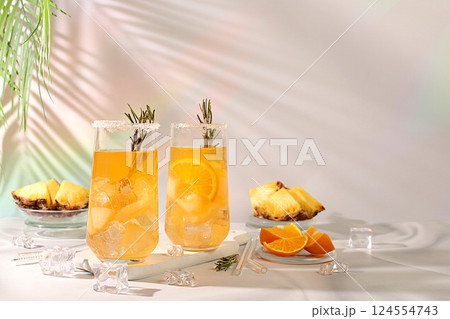 Summer party concept. Tequila, rum and vodka cocktail with pineapple slices, orange, ice and rosemary. Diet drink for detoxification and weight loss, bar or cafe advertisement, restaurant menu 124554743