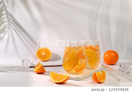 Orange juice and oranges on elegant kitchen table with long hard shadows. Modern still life with citrus fruits, minimal detox diet concept, summer vitamin drinks, selective focus, space for text 124554926