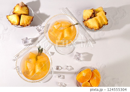 Cocktail with tequila, rum and vodka with pineapple slices, orange, ice and rosemary. Summer party concept. Diet drink for body detox and weight loss, advertising for a bar or cafe, menu for a 124555304