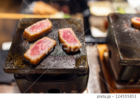 Gyukatsu slices cooking on a tabletop ceramic grill with sizzling juices and a golden-brown crust 124555851