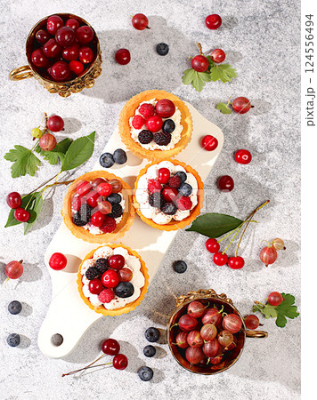Delicious tartlets with fresh berries raspberries, cherries, gooseberries and blueberries. Cupcakes with soft curd cream, summer dessert. Concept of a modern bakery, advertising for a cafe, 124556494