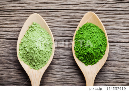 Green and light green spirulina and chlorella powders displayed on wooden spoons showcasing their vibrant colors and textures in a well-lit kitchen setting 124557419