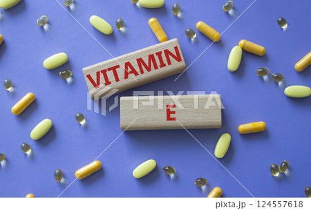 Vitamin E symbol. Concept word Vitamin E on wooden blocks. Beautiful purple background with pills. Medicine and Vitamin E concept. Copy space Vitamin E symbol. Concept word Vitamin E on wooden blocks. Beautiful purple background with pills. Medicine and Vitamin E concept. Copy space 124557618