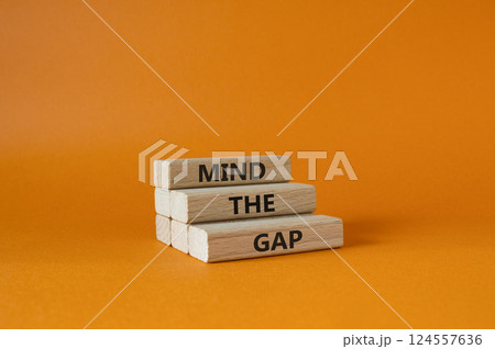 Mind the gap symbol. Concept words Mind the gap on wooden blocks. Beautiful orange background. Business and Mind the gap concept. Copy space. Mind the gap symbol. Concept words Mind the gap on wooden blocks. Beautiful orange background. Business and Mind the gap concept. Copy space. 124557636