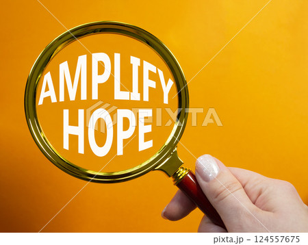 Amplify Hope symbol. Concept word Amplify Hope on magnifying glass. Businessman hand. Beautiful orange background. Business and Amplify Hope concept. Copy space 124557675