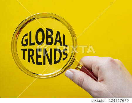 Global Trends symbol. Magnifying glass with words Global Trends. Businessman hand. Beautiful yellow background. Business and Global Trends concept. Copy space. 124557679