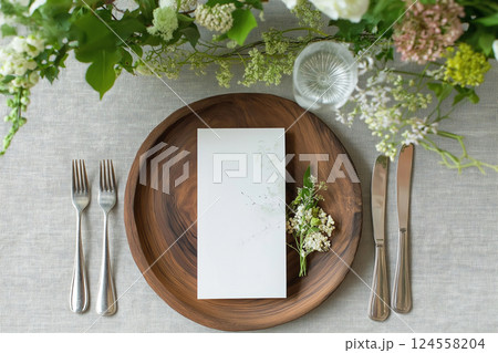 Elegant wedding table setting with menu card and floral decoration on wooden surface. Top view of a formal dining setup with flowers and a blank menu card. Empty card, mockup 124558204