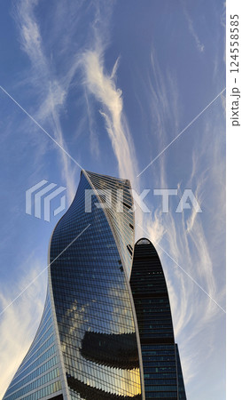 A stunning architectural skyscraper with a curvilinear design reflecting the blue sky and clouds, captured during golden hour. 124558585