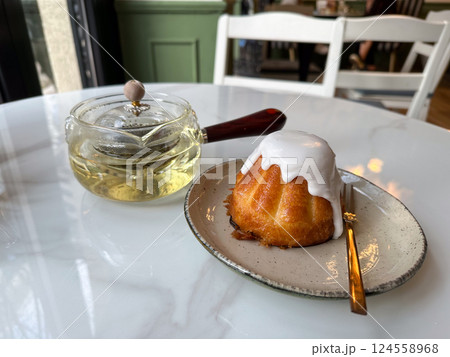 Sweet dessert with icing and glass teapot on white table in cafe. Peaceful leisure and warm tea break in a cozy setting Sweet dessert with icing and glass teapot on white table in cafe. Peaceful leisure and warm tea break in a cozy setting 124558968
