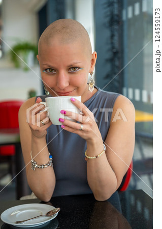 Young woman with cancer sitting in a cafe, drinking coffee and enjoying everyday life. The concept highlights that people with illnesses continue to live actively and socialize 124559173
