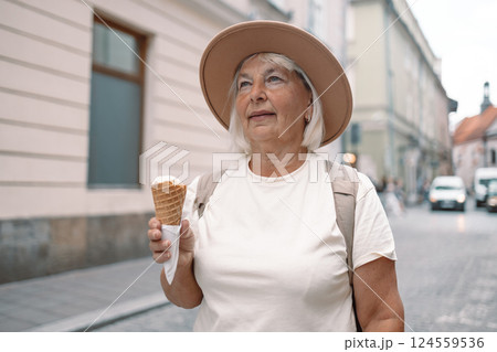 Senior woman walking down the street with an ice cream cone in hand, enjoying the moment. 124559536