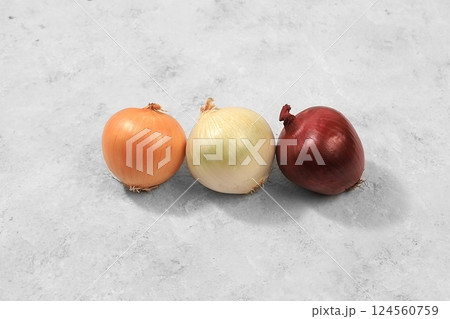 Various varieties of onions on a gray concrete background, the concept of harvesting in autumn, red, white and golden onions for breeding in agriculture, selective focus 124560759