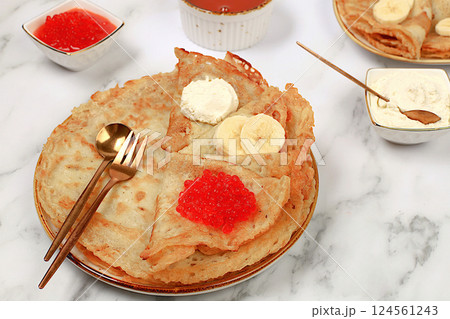 Delicious Russian pancakes with red caviar, soft cheese curd, bananas and honey on a marble table. Healthy breakfast with ingredients, carnival concept and traditional national cuisine, selective Delicious Russian pancakes with red caviar, soft cheese curd, bananas and honey on a marble table. Healthy breakfast with ingredients, carnival concept and traditional national cuisine, selective 124561243