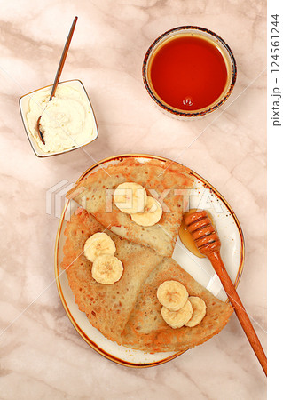 Delicious Russian pancakes with soft cheese, bananas and honey on a marble table. Healthy breakfast with ingredients, carnival concept and traditional national cuisine, selective focus 124561244