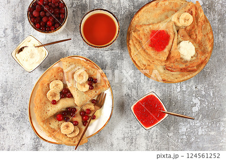 Delicious Russian pancakes with red caviar, soft cheese curd, bananas, cranberries and honey on a wooden table. Healthy breakfast with ingredients, carnival concept and traditional national cuisine, 124561252