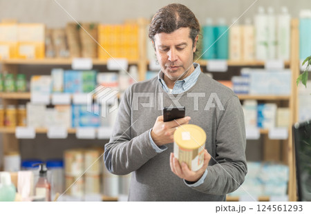 Male shopper in autumn clothes scans QR code on label of food for small children using smartphone 124561293