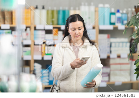 Middle-aged woman scanning QR-code on shampoo in drugstore 124561383