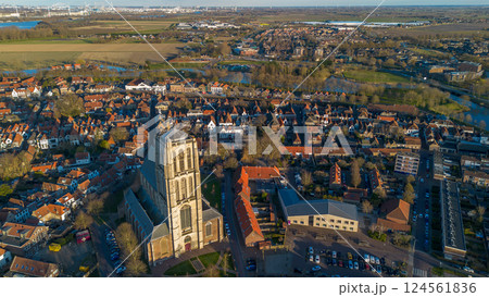 Aerial view of a historic town with a tall Gothic church in the center. Red-roofed houses, narrow streets, and a distant industrial skyline create a mix of old and modern architecture. 124561836