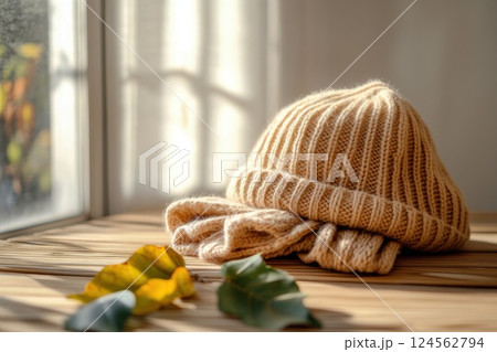 Soft wool hat resting on a wooden table beside autumn leaves in gentle daylight 124562794