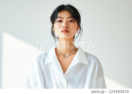 Model of East Asian descent showcases statement necklace in minimalist setting with natural light 124563019