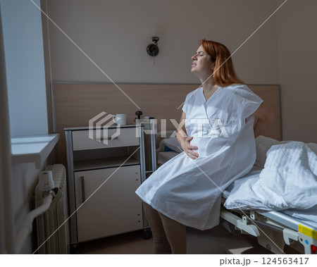 An unhappy pregnant woman sits on a couch in a hospital room. 124563417