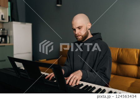 Concentrated male musician plying on electric piano, composing music at home, practicing and recording new song in stylish modern apartment setting. Concept of recording music at home. 124563434