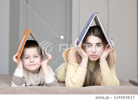 Concept home, family. Beautiful 19 year old girl and 5 year old boy lying on bed holding books above their heads in shape of house. 124563617