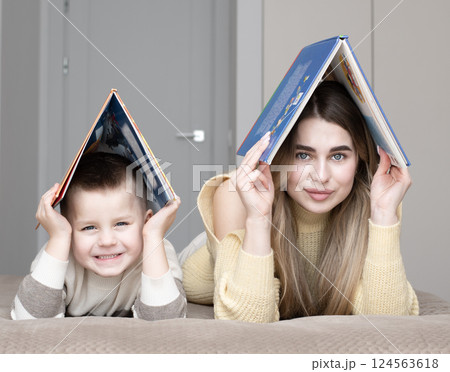 Concept home, family. Beautiful 19 year old girl and 5 year old boy lying on bed holding books above their heads in shape of house. 124563618